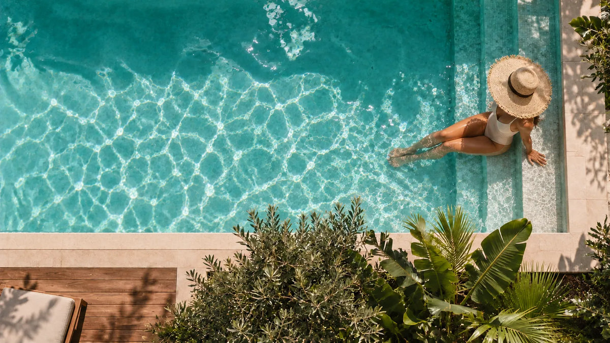 Woman in a straw hat sitting on the steps of a sunlit turquoise magnesium pool