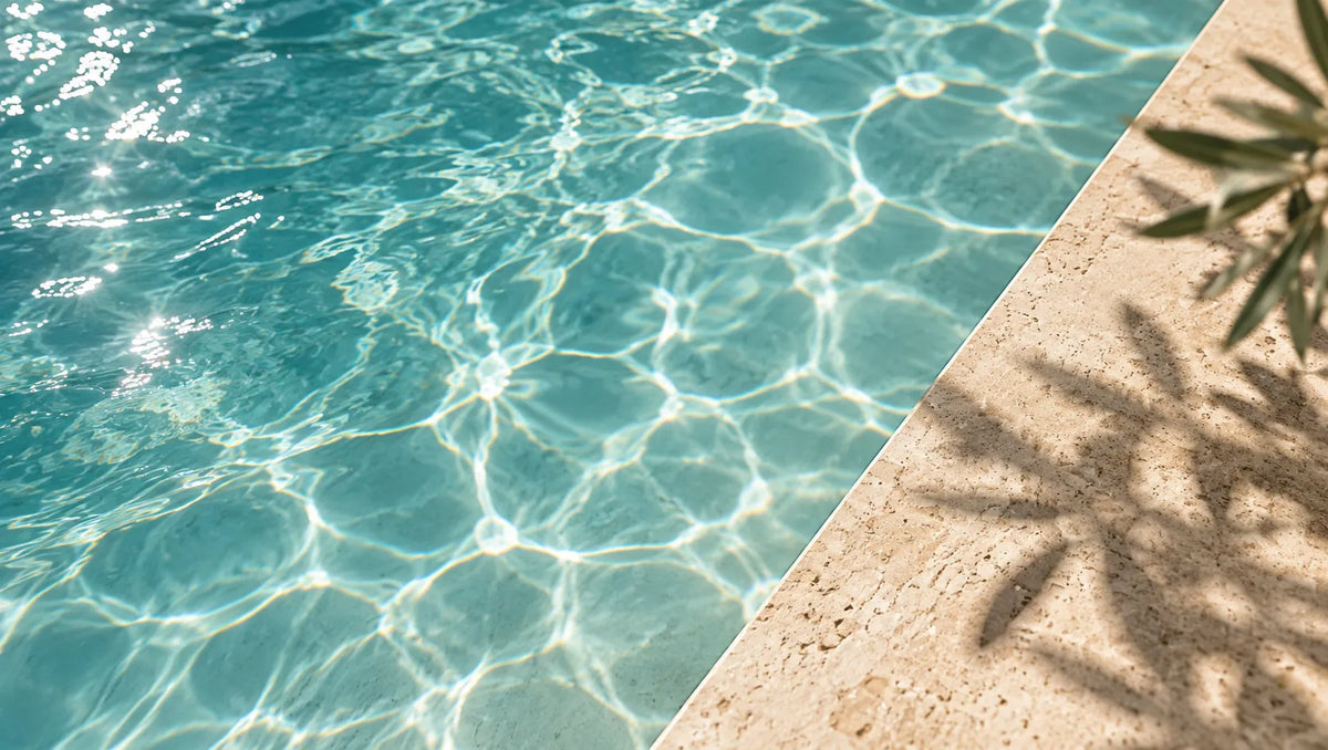 Sunlit turquoise pool water beside a travertine edge with palm shadows
